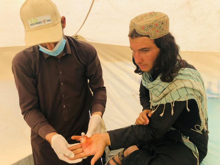 A man is treated for a wound on his hand in the HealthNet TPO treatment tent, in Mohammadi village, Khost Province. Photo: UNHCR/Mohammad Haroon